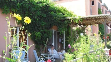 Un área de estar al aire libre con una mesa y sillas, rodeada de abundante vegetación y flores.