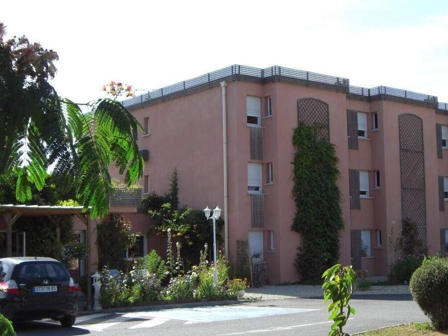 Un edifici de diverses plantes amb façana rosa, grans finestres i una entrada tancada per una reixa.