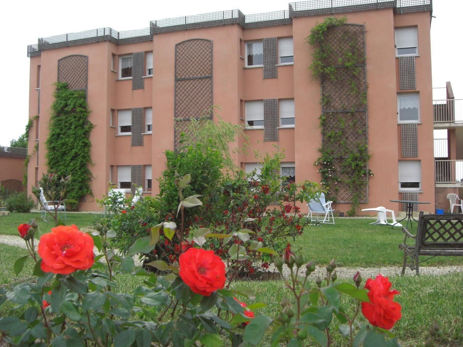 Un immeuble à plusieurs étages doté de balcons, un jardin avec des fleurs rouges et des espaces de repos en plein air.