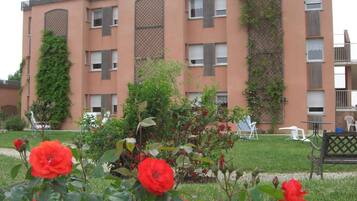 Un immeuble à plusieurs étages doté de balcons, un jardin avec des fleurs rouges et des espaces de repos en plein air.