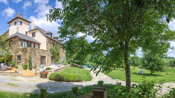 A stone house with a patio, surrounded by lush greenery and a clear sky. - L'ecrin du Segala - La roulotte (Tauriac-de-Naucelle)