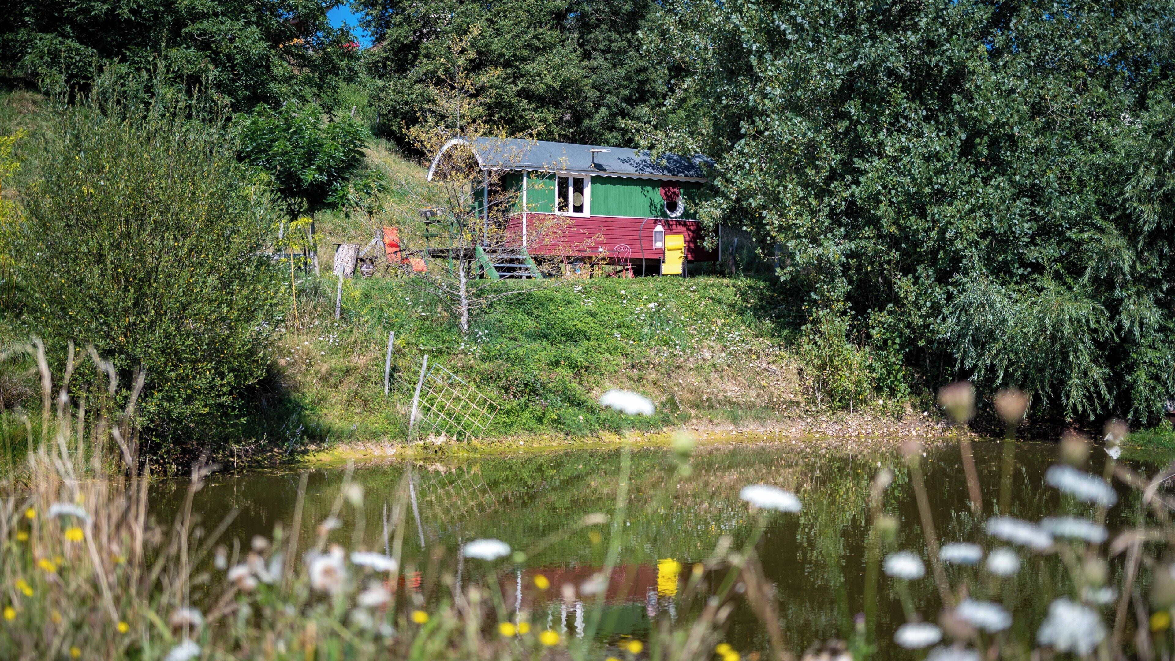 Una casa de techo rojo y paredes verdes, rodeada de abundante vegetación y una masa de agua.