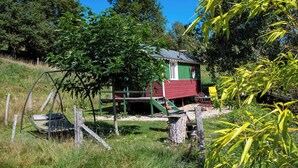 A rustic wooden house with a green roof, surrounded by lush greenery and a swing set. - L'ecrin du Segala - La roulotte (Tauriac-de-Naucelle)