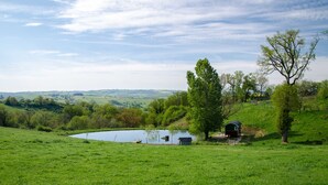 A serene landscape with a pond, a small building, and a tree. - L'ecrin du Segala - La roulotte (Tauriac-de-Naucelle)