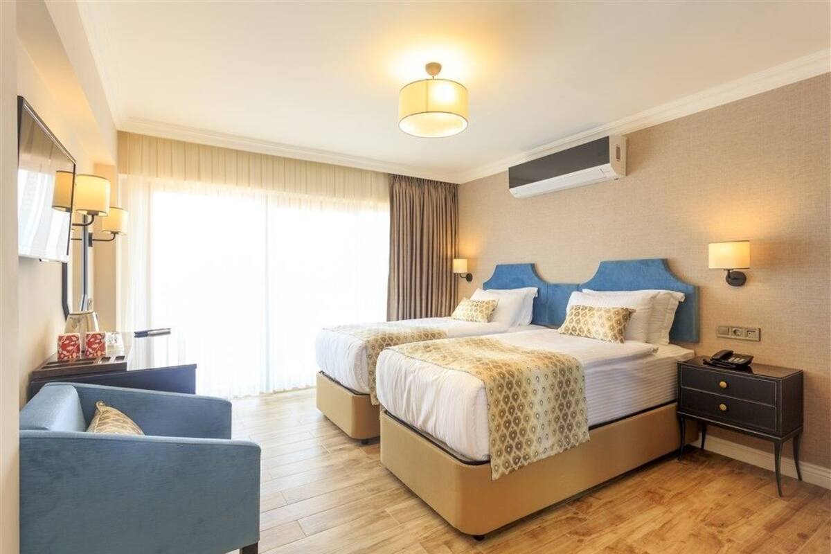 Une chambre d’hôtel avec deux lits, un bureau, une chaise et une grande fenêtre avec des rideaux.