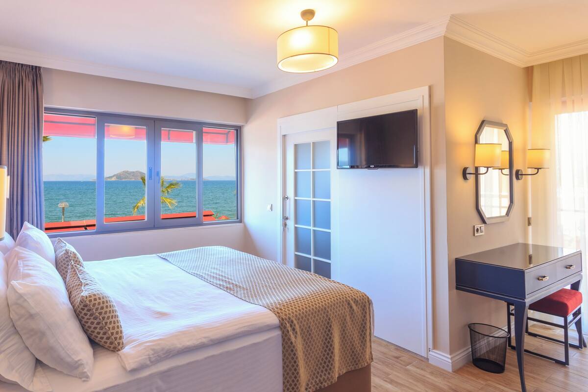 Une chambre d’hôtel avec un lit, un bureau, une télévision et une fenêtre donnant sur la mer.