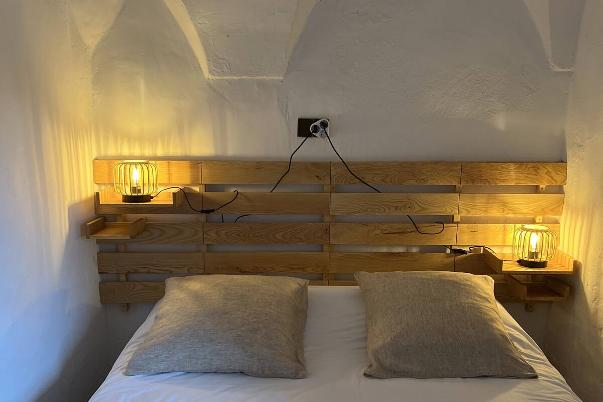 Ein Schlafzimmer mit einem hölzernen Kopfteil, zwei Nachttischen mit Lampen und einem Bett mit zwei Kissen.