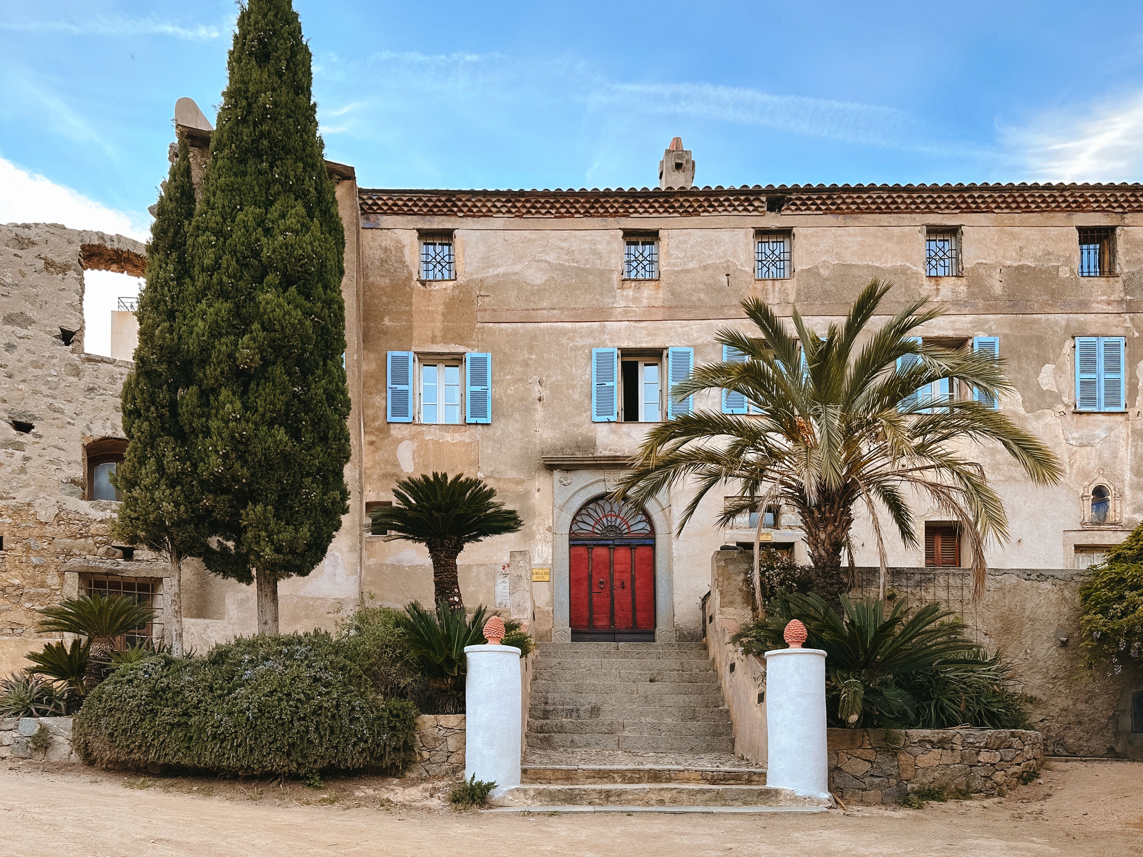 A historic building with a red door, blue shutters, and a stone staircase leading to the entrance.