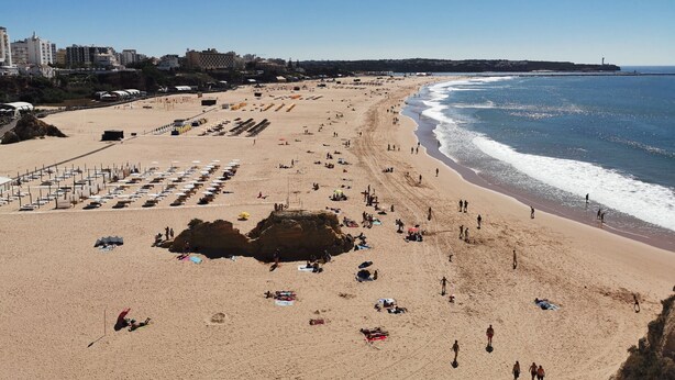 A wide beach with a rocky outcrop in the center, a pier on the left, and buildings in the background. - Apartment Praia Rocha Justar Cozy (Portimão)