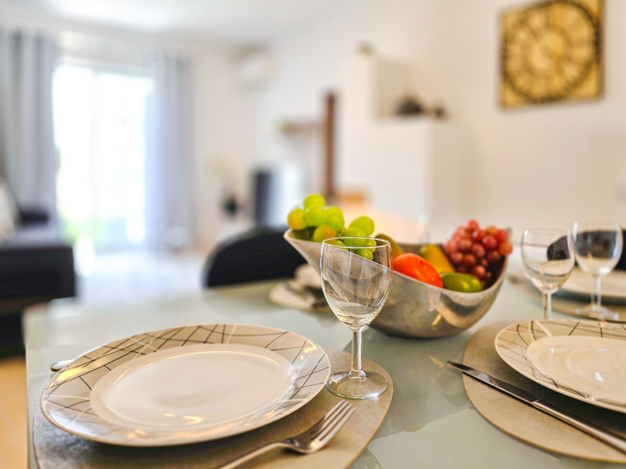 A dining table set with plates, a wine glass, and a bowl of fruit.