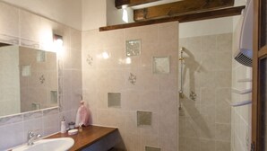 Ein Badezimmer mit einem Holzbadezimmerhocker, einem großen Spiegel, einer Dusche und einem kleinen Schrank.