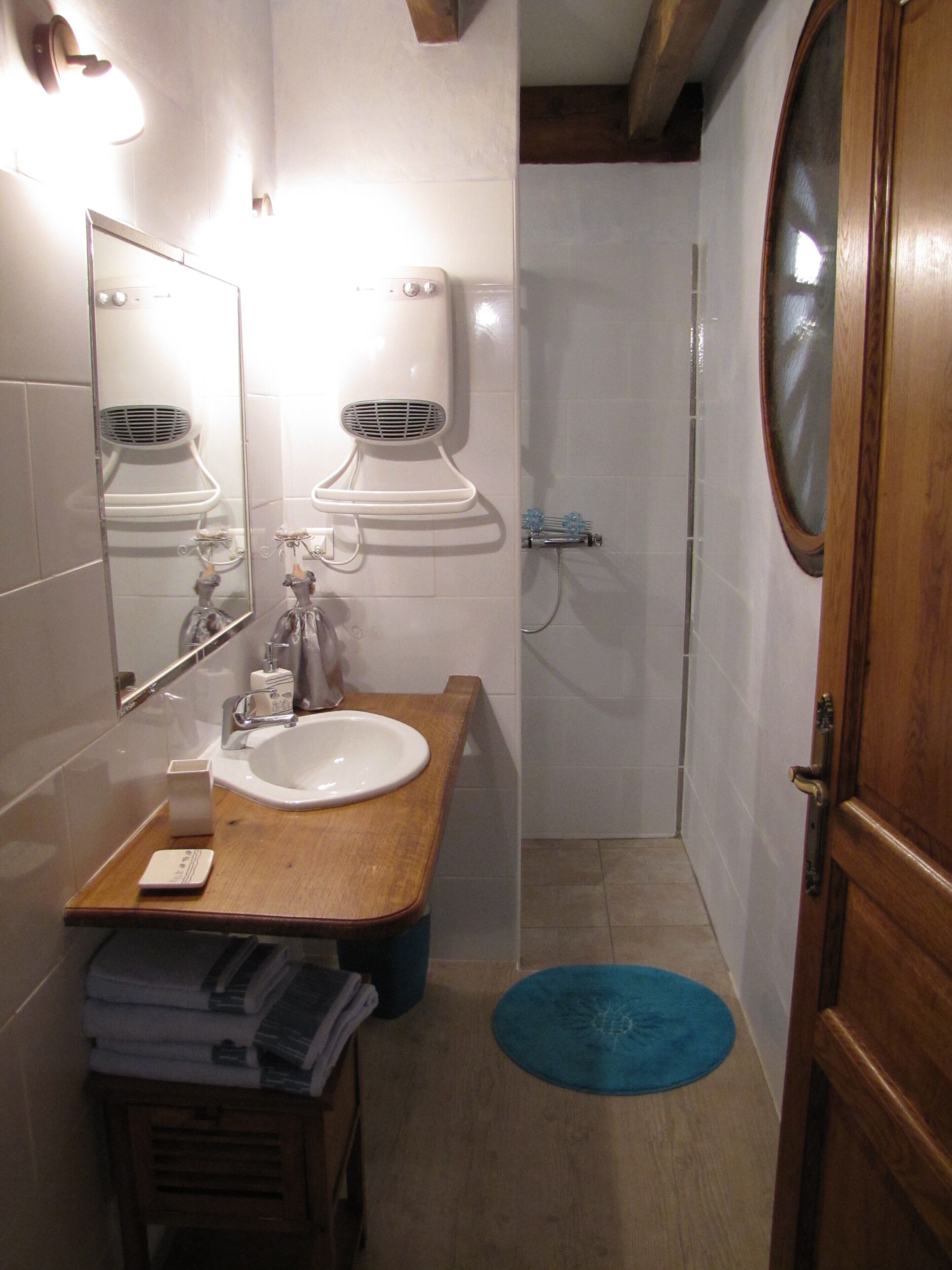 A bathroom with a wooden vanity, a sink, a mirror, a towel rack, and a shower area.