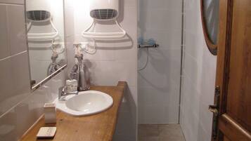 A bathroom with a wooden vanity, a sink, a mirror, a towel rack, and a shower area.