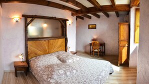 Ein Schlafzimmer mit hölzernem Kopfteil, einem Bett mit floralem Bettzeug, einem Nachttisch, einem Stuhl, einem kleinen Tisch und einem Kleiderschrank.