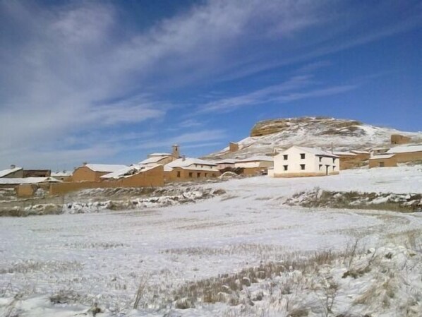 Paisaje nevado con edificios y una colina al fondo.