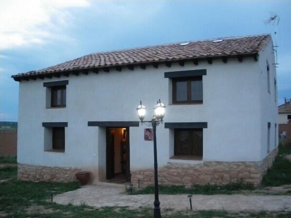 A two-story building with a tiled roof, a stone base, and a small front porch with two wall-mounted lights.