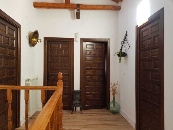 Un pasillo con puertas de madera, un radiador, una mesita y una planta colgante.