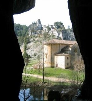 A small building with a tiled roof, surrounded by greenery and a rocky landscape.