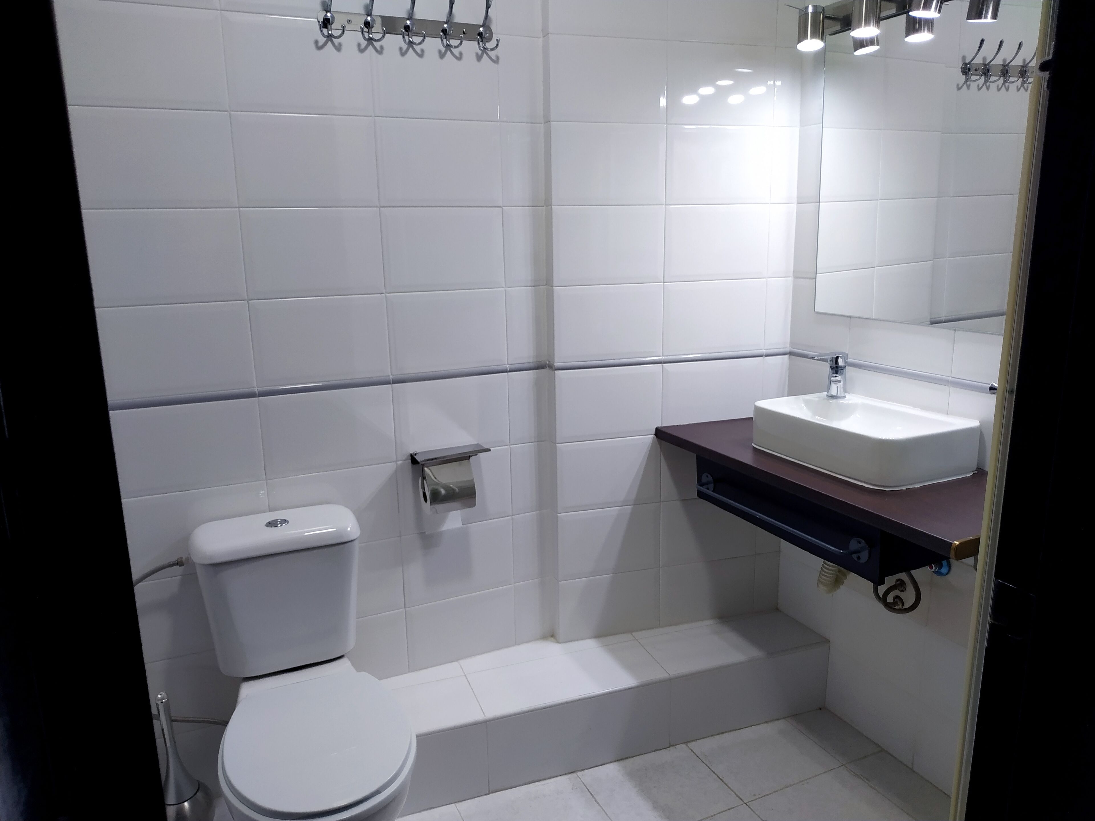 A modern bathroom with white tiles, a white toilet, a sink with a mirror, and a shower area.