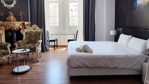 Una habitación de hotel con una cama grande, una zona de estar con sofá y sillones, una mesita y una chimenea decorativa.