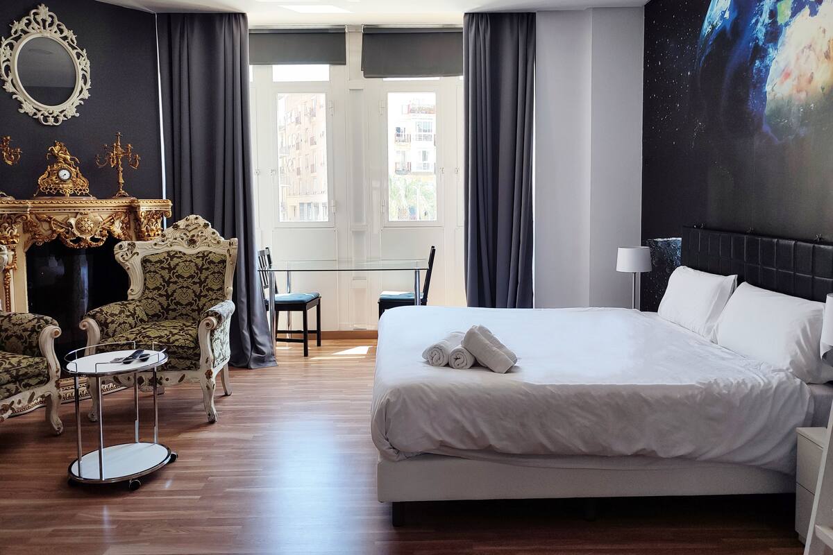 Een hotelkamer met een groot bed, een zithoek met een bank en stoelen, een kleine tafel en een decoratieve openhaard.