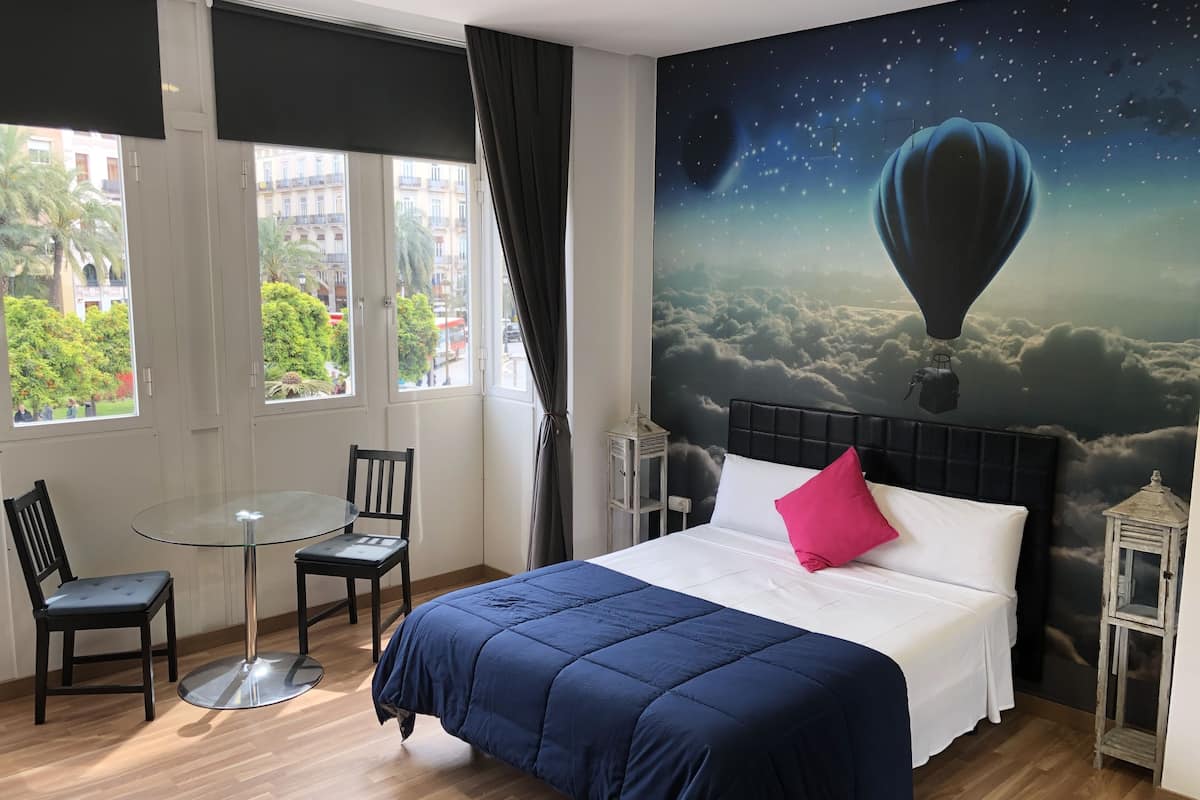 Een hotelkamer met een groot bed, een glazen tafel, twee stoelen en een muurschildering van een luchtballon.