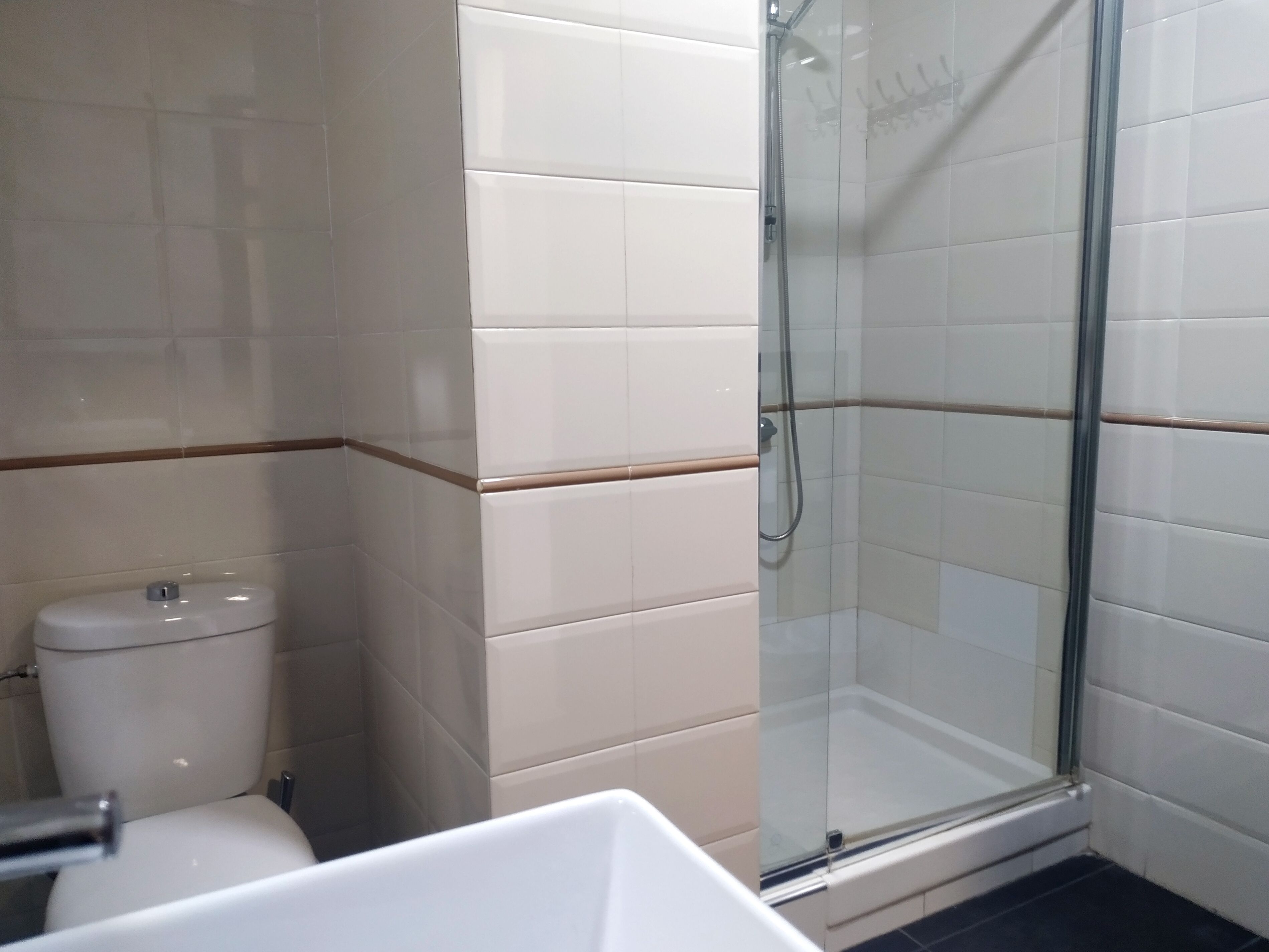 A bathroom with a toilet, a glass shower enclosure, and white tiled walls.