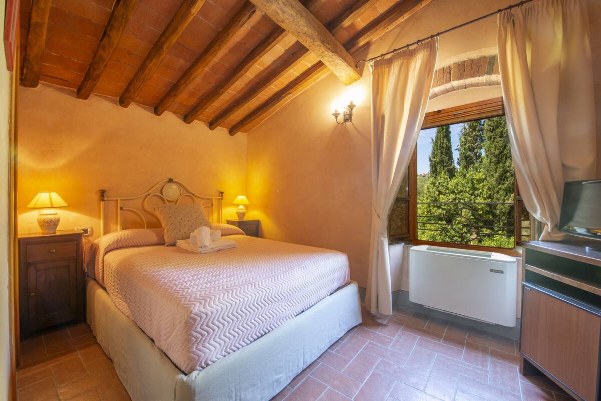 A bedroom with a bed, bedside lamps, a window with curtains, and a radiator.
