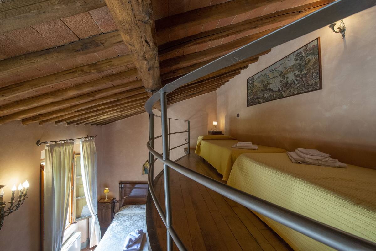 A rustic room with a bunk bed, wooden beams, a painting on the wall, and a window with curtains.