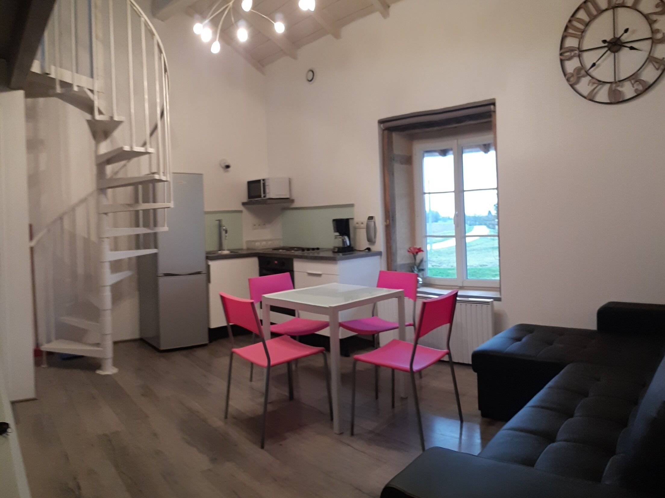 A compact kitchen with a dining area, a staircase, and a view through a window.
