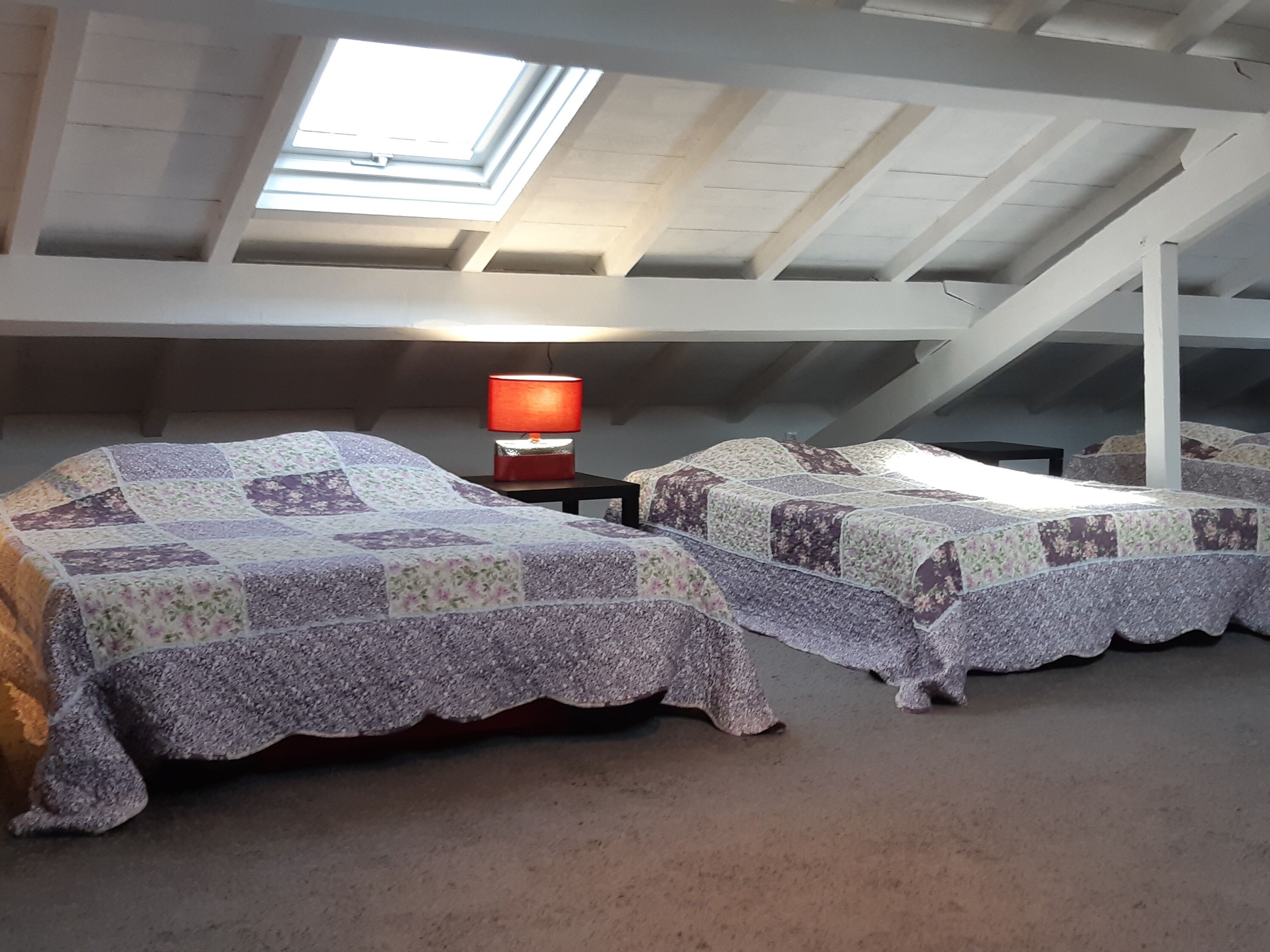 Ein Schlafsaalzimmer mit zwei Betten, einem Dachfenster und einem Tisch mit einer Lampe.
