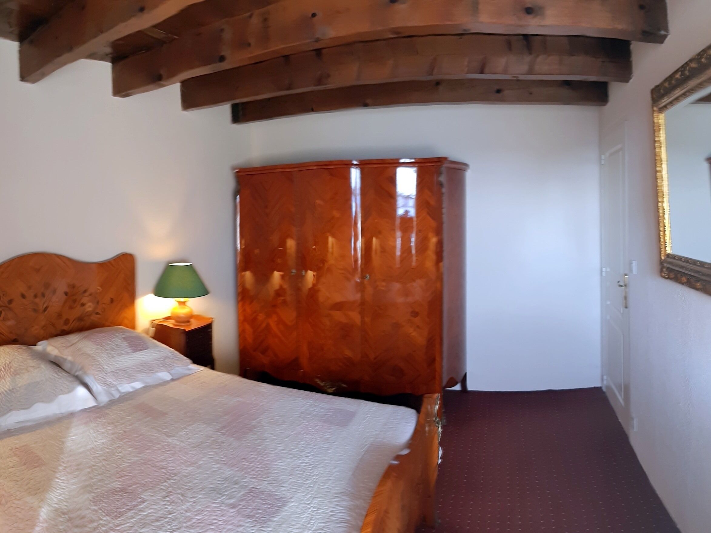 Ein Schlafzimmer mit einem hölzernen Kopfteil, einem großen Holzschrank, einer grünen Lampe und einem roten Teppich.