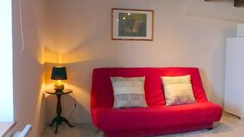 Un canapé rouge avec des coussins à motifs, une petite table avec une lampe et un tableau encadré au mur.