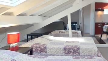 Un dormitorio con techo inclinado, una cama con colcha floral, una mesita de noche con lámpara roja y una escalera que conduce a un nivel superior.