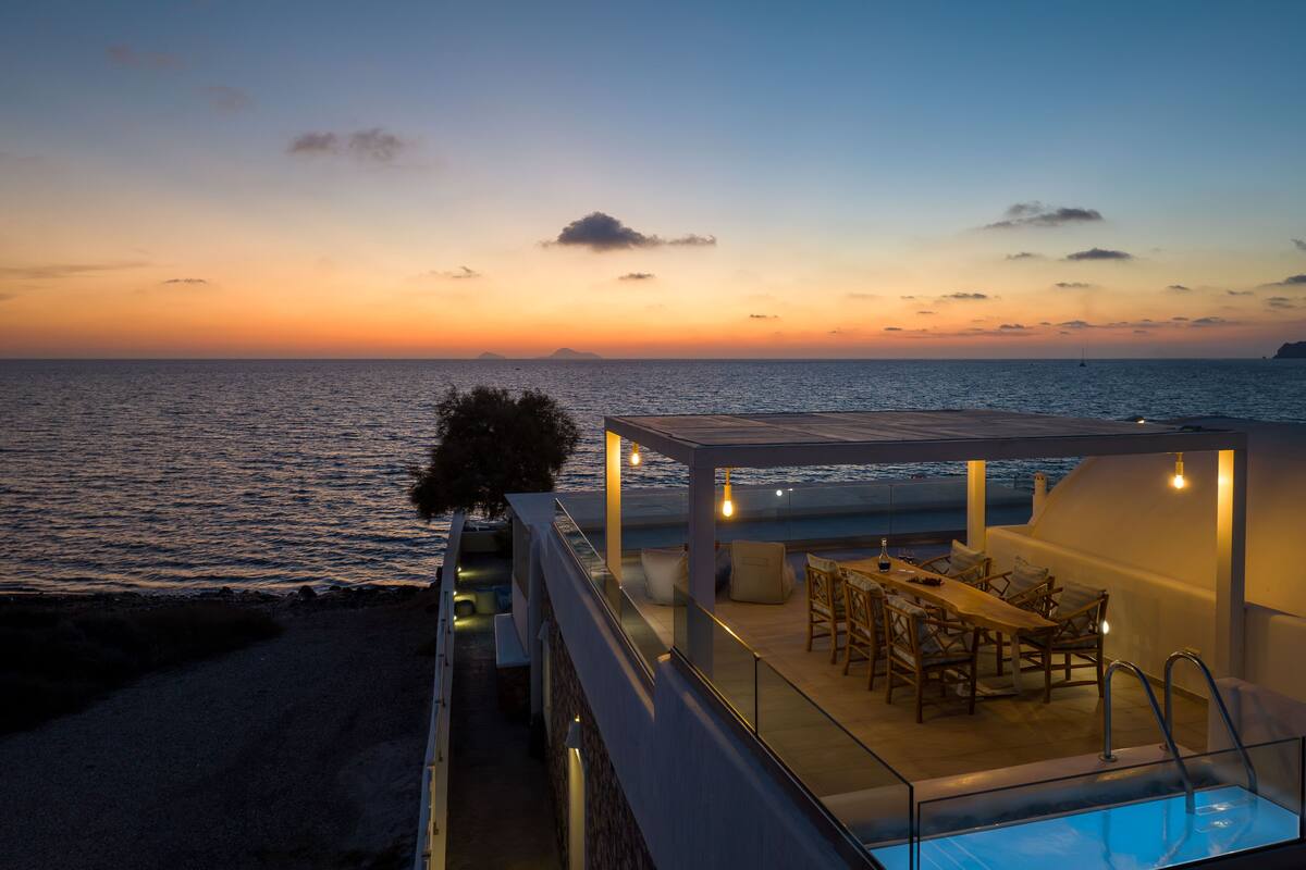 A rooftop terrace with a pool, dining area, and ocean view at sunset.