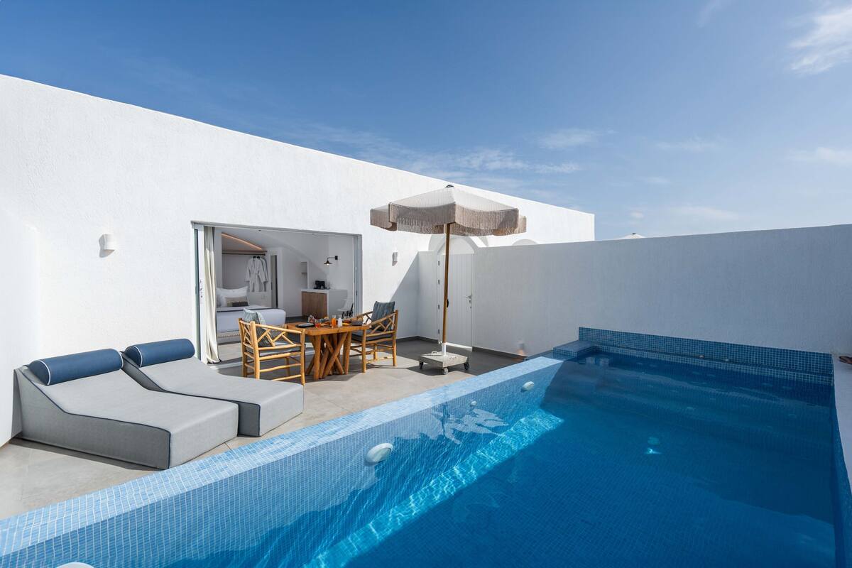A modern outdoor pool area with a seating area, a wooden table, and an umbrella.