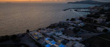 An aerial view of a coastal town at sunset with a marina, buildings, and a clear view of the sea.