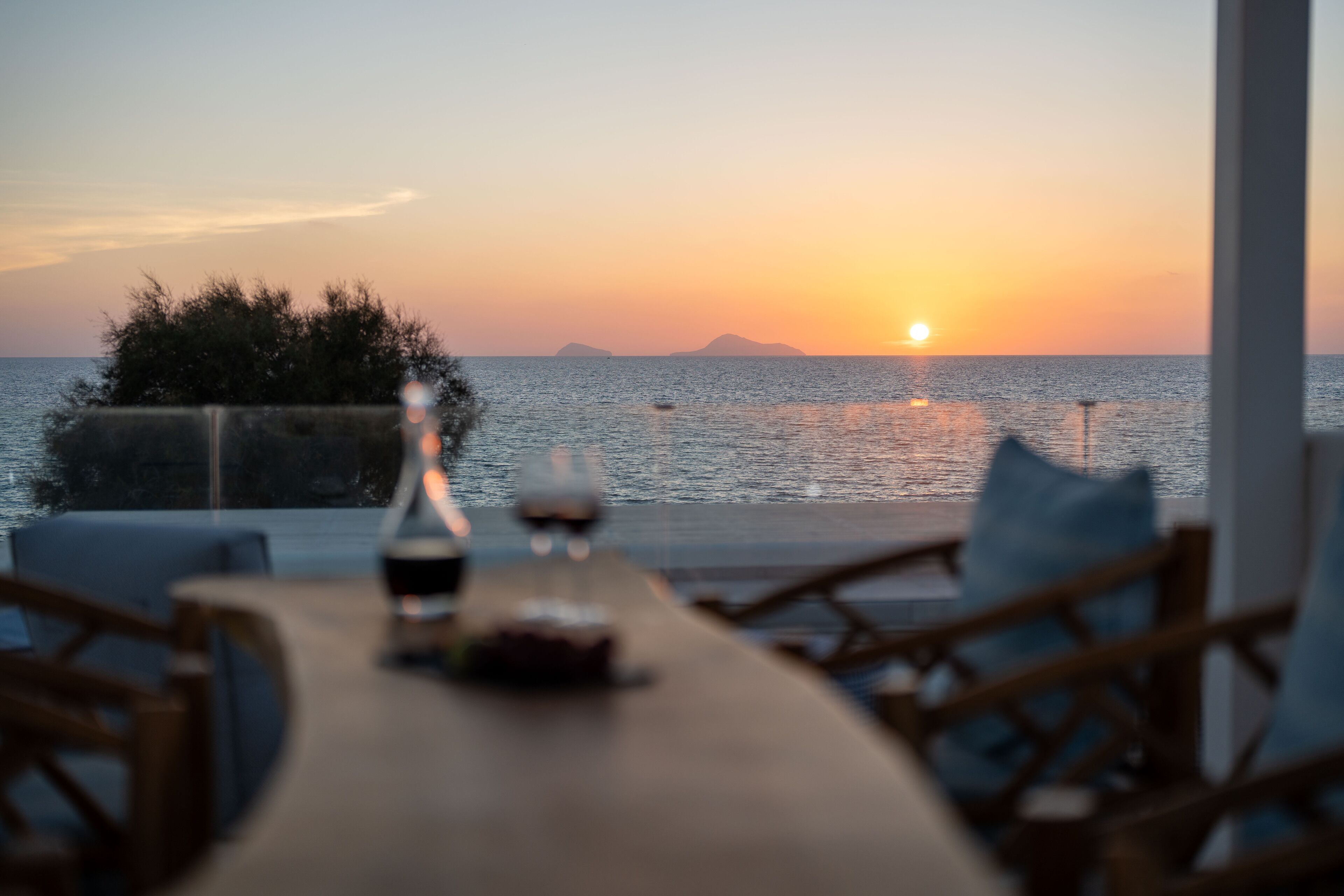 Una mesa con sillas y vistas al atardecer sobre el mar.