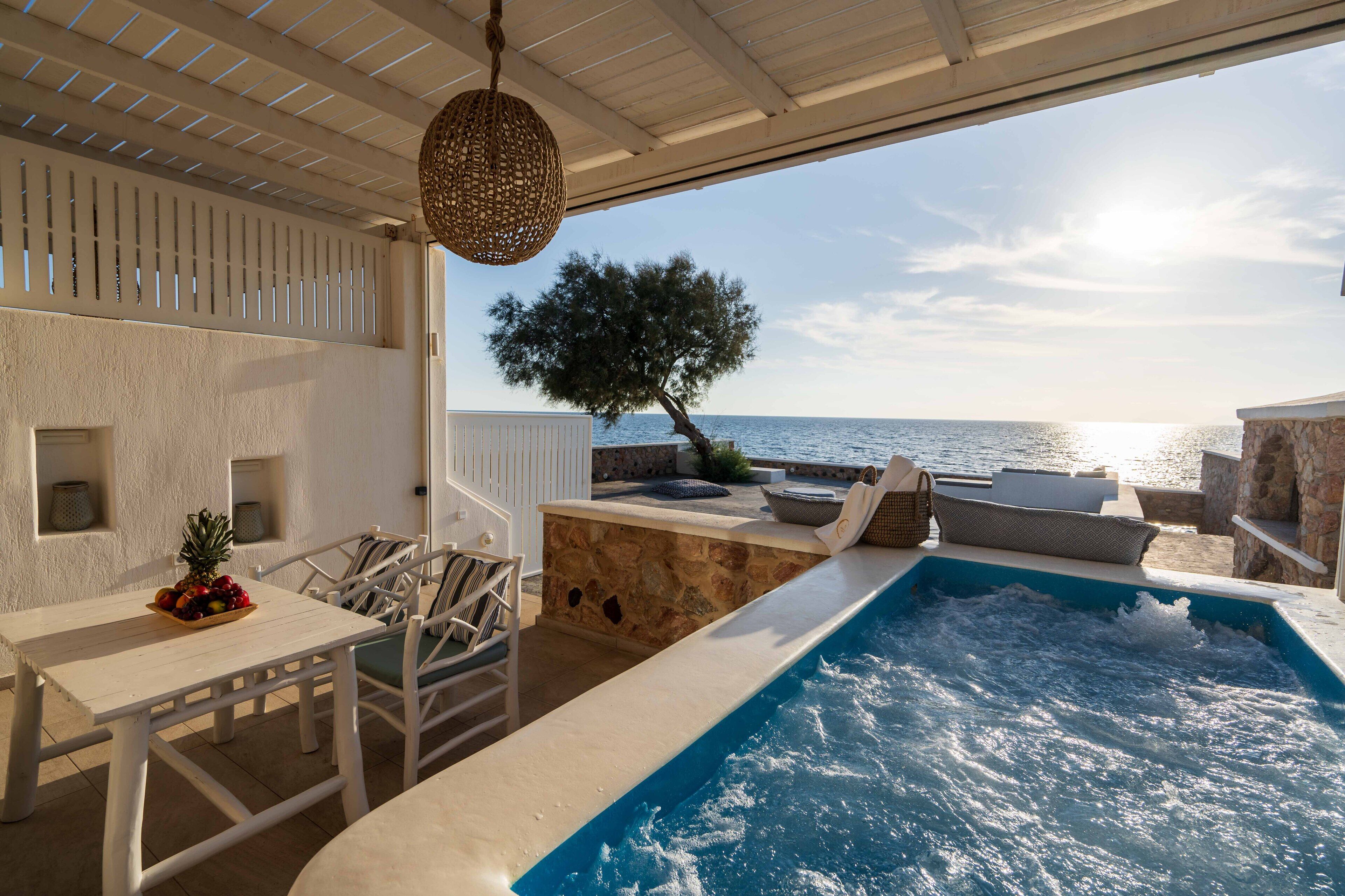A pool area with a view of the sea, stone walls, and outdoor seating.