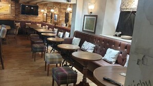 A cozy restaurant with wooden tables, cushioned seating, and a brick wall backdrop. - Queen Catherine Hotel (Northallerton)