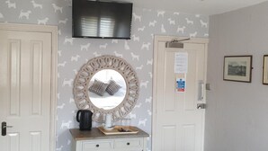 A room with two doors, a television mounted on the wall, a decorative mirror, and a small table with a coffee maker and a tray. - Queen Catherine Hotel (Northallerton)