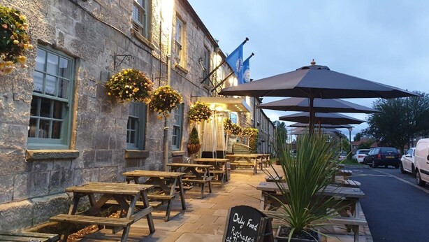 A stone building with outdoor seating and umbrellas. - Queen Catherine Hotel (Northallerton)