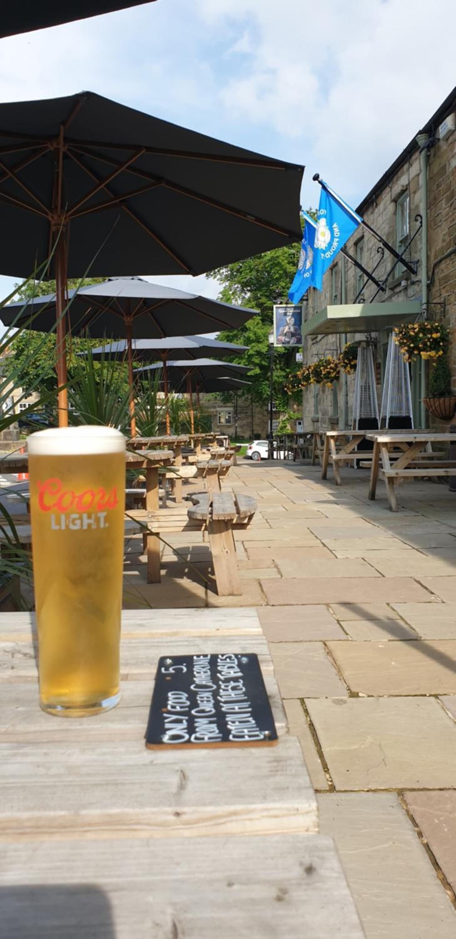 Coors Light -oluttölkki puupöydällä, jonka vieressä on liitutaulusta tehty ruokalista.