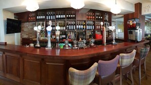 A bar area with a wooden counter, multiple taps, and a selection of bottled beverages. - Queen Catherine Hotel (Northallerton)