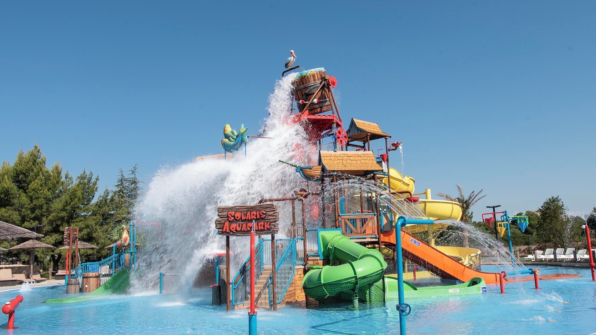 A water park with a large water slide, a sign reading "Solaris Aquapark," and a pool area.