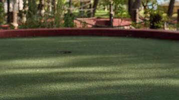 Una pallina da golf su un tappeto verde, con alberi e una recinzione sullo sfondo.