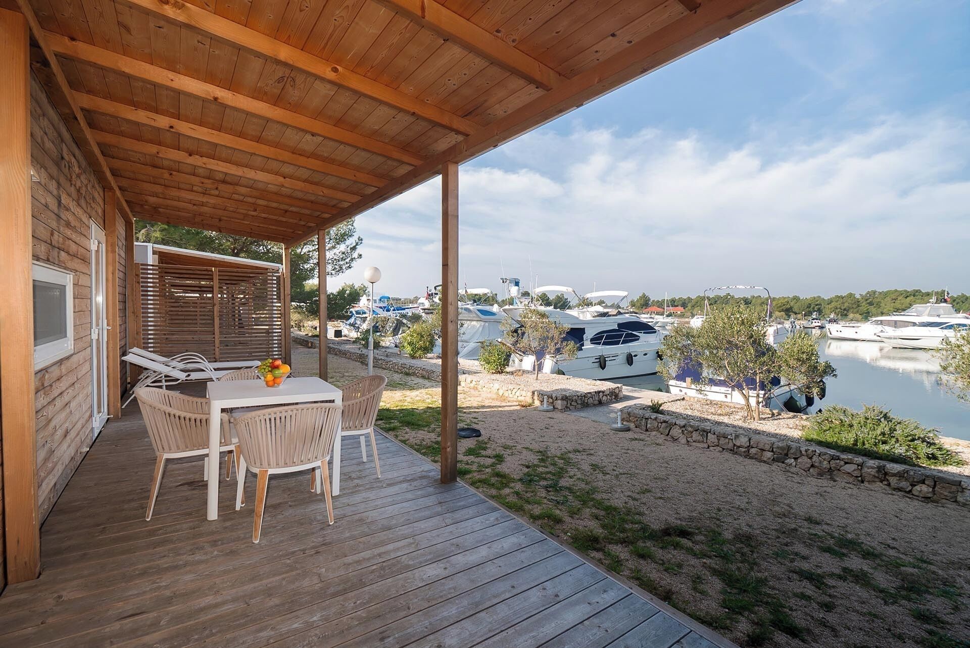 A wooden deck with a table and chairs, overlooking a marina with boats.
