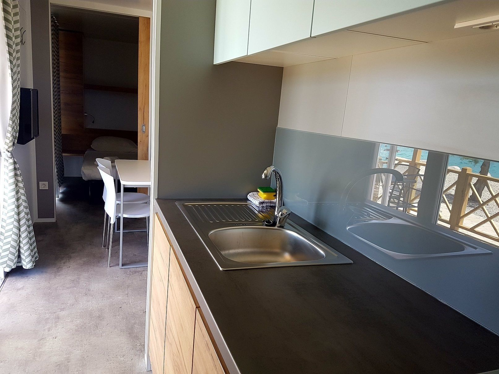 A compact kitchen with a sink, a small dining area with chairs, and a view of the sea through a window.