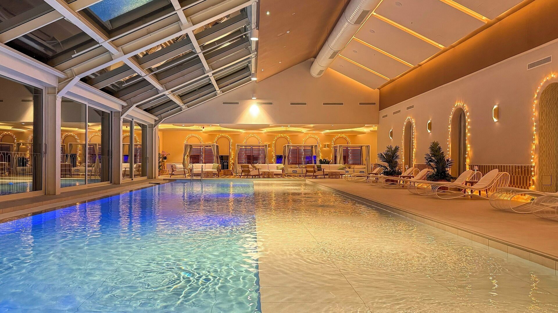 An indoor swimming pool with clear water, surrounded by lounge chairs and a seating area with a view of the pool.