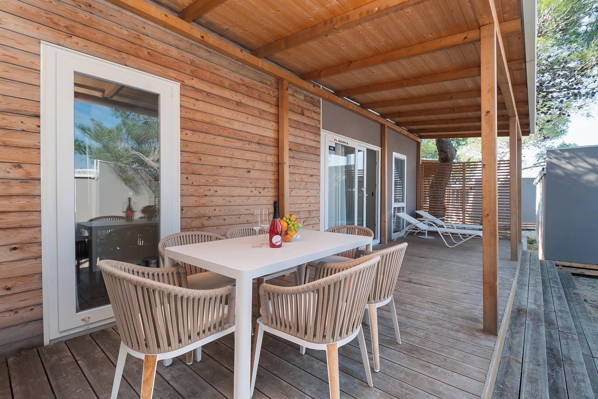 Un espace extérieur abrité, doté d’une table et de chaises, d’une porte vitrée et d’une terrasse en bois.